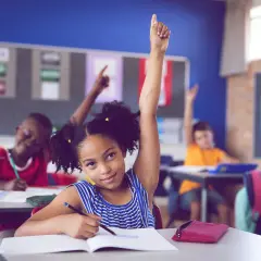 Ein Mädchen hebt im Unterricht die Hand. Viele Kinder lernen, was die bilingualer unterricht vorteile nachteile mit sich bringt.
