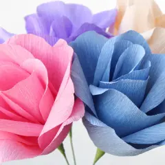 Bunte Papierblumen, die zum Basteln einladen. Eine rosa, blaue und lila Blüte sind zu sehen.