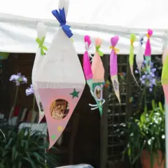 Bunte Zuckertüten mit Fotos hängen im Garten. Perfekte Spiele zur Einschulung im Garten für einen unvergesslichen Tag.