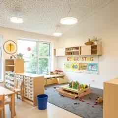 Helle, kindgerechte Reggio Raumgestaltung Kita mit Holzelementen, Spielzeug und einem Geburtstagsbanner.