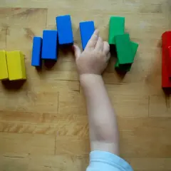 Ein Kinderarm greift nach bunten Holzklötzen. So lernen Kinder spielerisch Farben kennen: Gelb, Blau, Grün und Rot.
