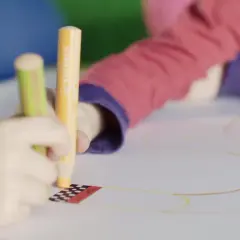 Kinder üben das Schreiben und Malen mit bunten Stiften auf einem großen Blatt Papier.