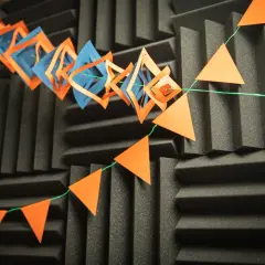Eine selbstgebastelte Girlande aus orangefarbenen Dreiecken und blauen Rauten hängt vor einer schwarzen Akustikwand.