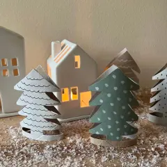 Kleine Weihnachtsbäume aus Papier, die Kinder basteln könnten, stehen vor leuchtenden Häusern.