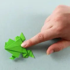 Grüner Origami-Frosch, der von einer Hand gehalten wird. Ein tolles Bastelprojekt für origami kinder.