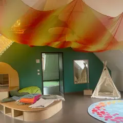 Ein gemütlicher Snoezelraum Kita mit bunten Decken, einem Spielhaus, einer Tipizelt und Lichterketten.