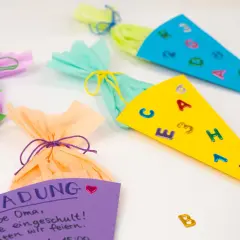 Bunte Schultüten und eine Einladung zum Einschulungsfest basteln. Kleine Buchstaben und Zahlen zieren die Tüten.