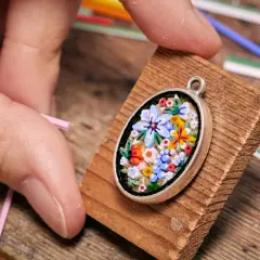 Ein zartes Blumen-Mosaik, einfach und detailreich, wird von Fingern gehalten. Kleine Glasstäbchen liegen bereit.