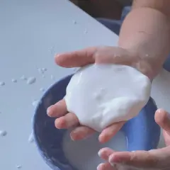 Kinderhände spielen mit weißer, klebriger Masse, die wie Oobleck-Rezept aussieht.