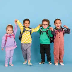 Vier fröhliche Kinder mit Rucksäcken, bereit für die Schule. Ein kleiner Junge mit kariertem Pullover scheint begeistert, vielleicht ist er ein **kind vorzeitig einschulen**?