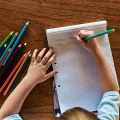 Kind schreibt Namen auf Papier, Teil der schuleingangsuntersuchung was wird gemacht. Buntstifte liegen bereit.