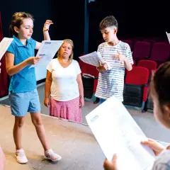 Kinder üben für ein **Vorlesetheater Grundschule**. Sie halten Texte in der Hand und schauen konzentriert.