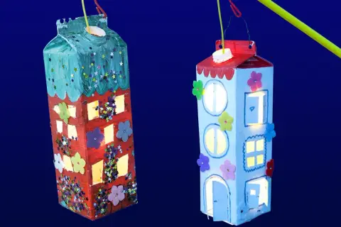Zwei selbstgebastelte Laternen in Hausform, leuchten im Dunkeln. Kinder haben hier ihre Kreativität beim Laternen basteln gezeigt.