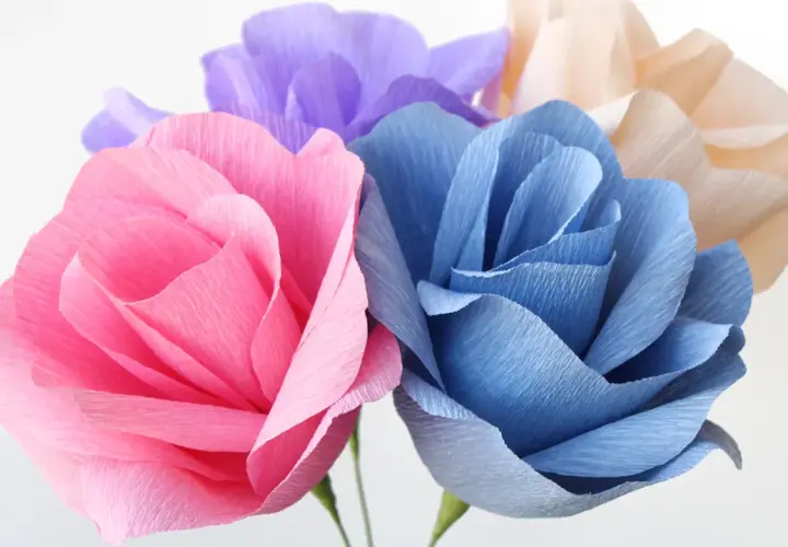 Bunte Papierblumen, die zum Basteln einladen. Eine rosa, blaue und lila Blüte sind zu sehen.