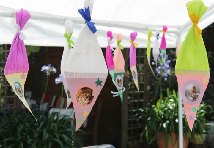 Bunte Zuckertüten mit Fotos hängen im Garten. Perfekte Spiele zur Einschulung im Garten für einen unvergesslichen Tag.