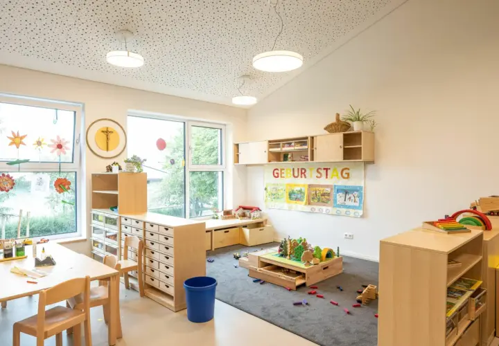 Helle, kindgerechte Reggio Raumgestaltung Kita mit Holzelementen, Spielzeug und einem Geburtstagsbanner.