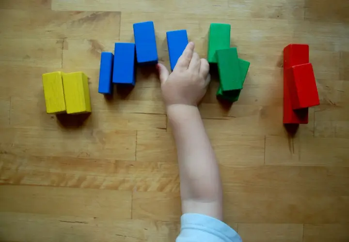 Ein Kinderarm greift nach bunten Holzklötzen. So lernen Kinder spielerisch Farben kennen: Gelb, Blau, Grün und Rot.