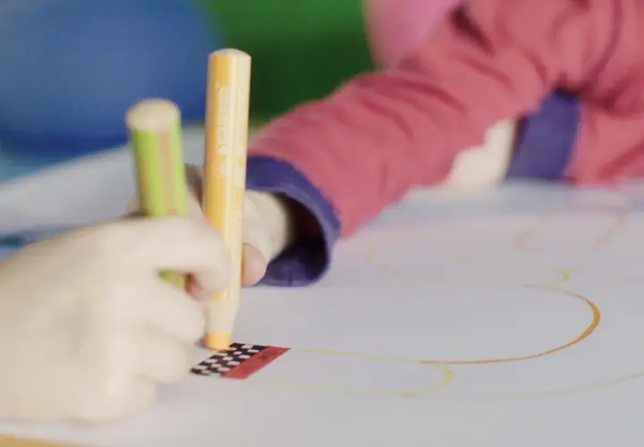 Kinder üben das Schreiben und Malen mit bunten Stiften auf einem großen Blatt Papier.