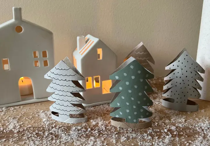 Kleine Weihnachtsbäume aus Papier, die Kinder basteln könnten, stehen vor leuchtenden Häusern.