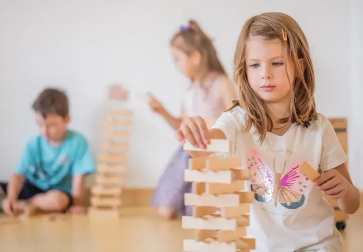 Kinder bauen in der Bauecke im Kindergarten einen hohen Turm aus Holzklötzen.