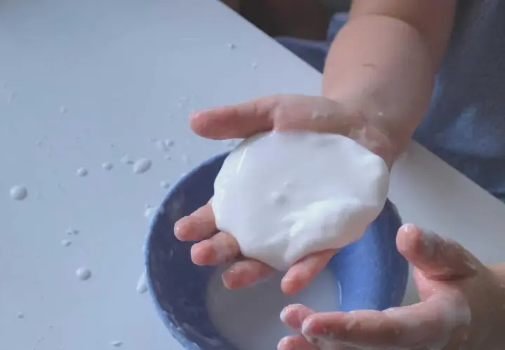 Kinderhände spielen mit weißer, klebriger Masse, die wie Oobleck-Rezept aussieht.
