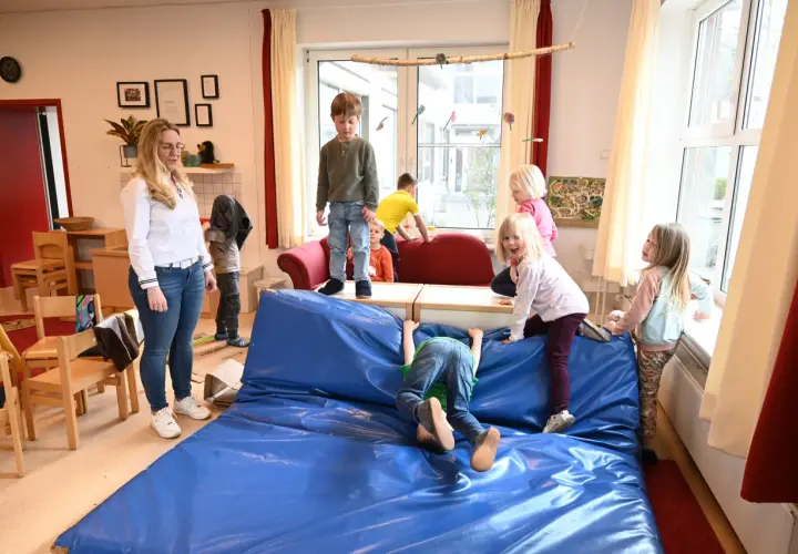 Kinder genießen spielzeugfreie Zeit in der Kita, klettern und toben auf einer blauen Matte.