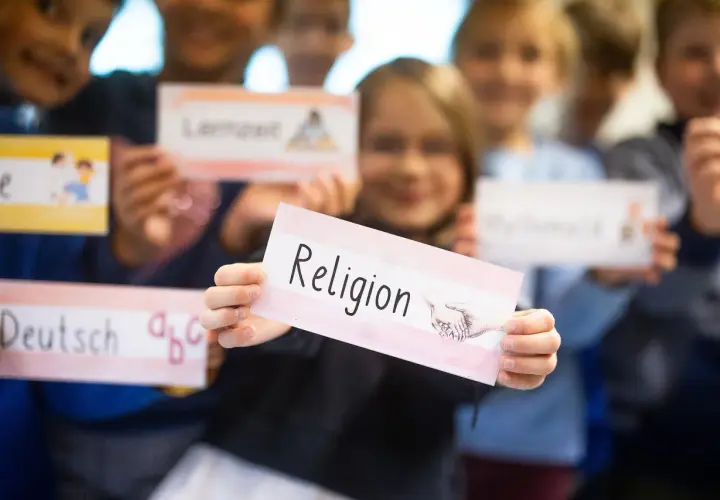 Kinder der Grundschule halten Schilder hoch, eines davon mit "Religion" beschriftet. Sie lernen über verschiedene Fächer, vielleicht im Rahmen der Fastenzeit.
