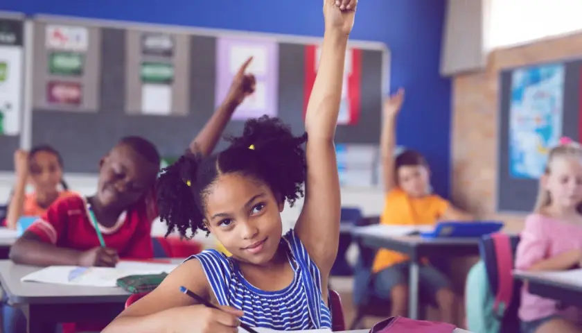 Ein Mädchen hebt im Unterricht die Hand. Viele Kinder lernen, was die bilingualer unterricht vorteile nachteile mit sich bringt.