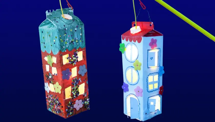 Zwei selbstgebastelte Laternen in Hausform, leuchten im Dunkeln. Kinder haben hier ihre Kreativität beim Laternen basteln gezeigt.