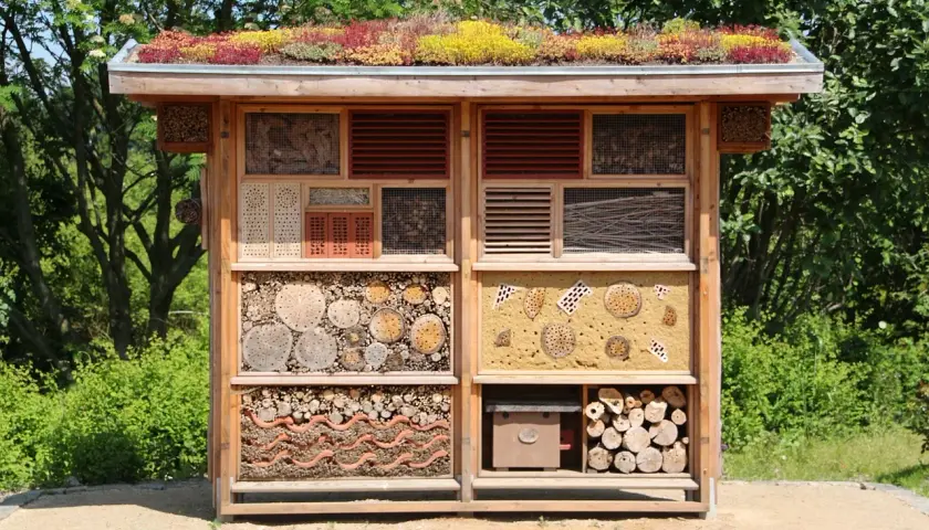 Ein großes Insektenhotel, das Kinder selber bauen können, mit vielen Fächern für verschiedene Insekten. Das Dach ist begrünt.