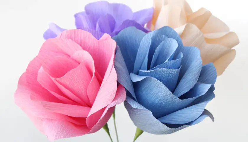 Bunte Papierblumen, die zum Basteln einladen. Eine rosa, blaue und lila Blüte sind zu sehen.