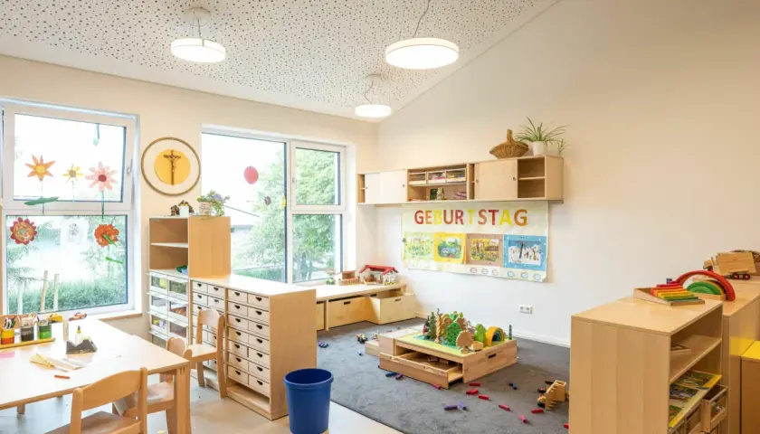 Helle, kindgerechte Reggio Raumgestaltung Kita mit Holzelementen, Spielzeug und einem Geburtstagsbanner.