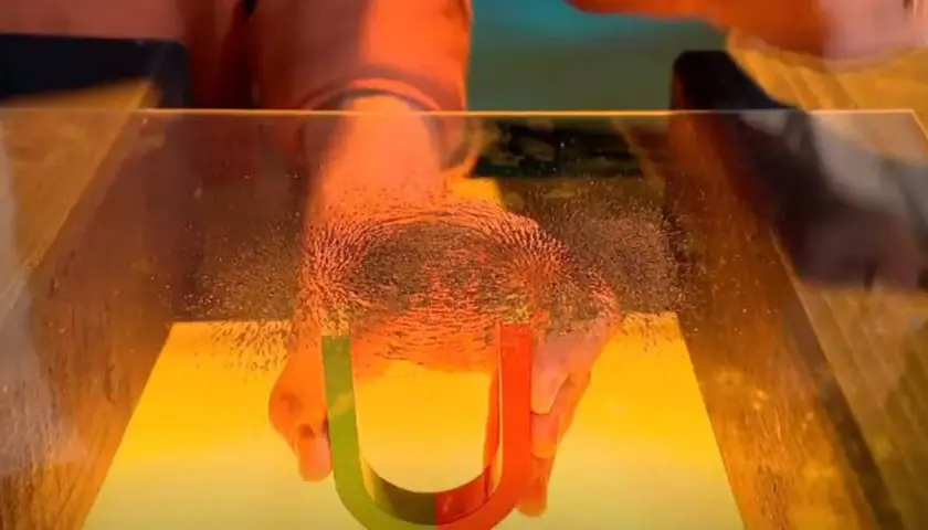 Hände halten Hufeisenmagnet, der Eisenpulver für Magnetismus-Experimente anzieht.