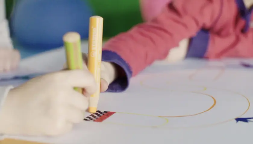 Kinder üben das Schreiben und Malen mit bunten Stiften auf einem großen Blatt Papier.