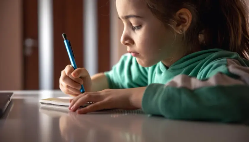 Ein Mädchen konzentriert sich auf das Nachspuren von Buchstaben in ihrem Heft, eine typische Übung für die Grundschule.