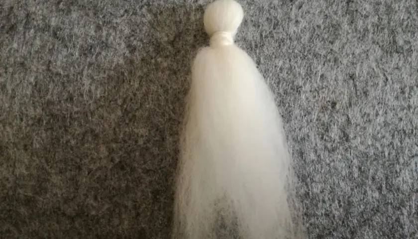 Ein weißer Wattebausch, der wie ein Kopf und ein Kleid aussieht, liegt auf grauem Filz. Dies ist der Anfang vom engel filzen.