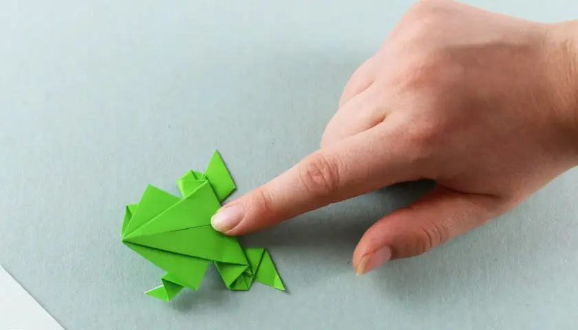 Grüner Origami-Frosch, der von einer Hand gehalten wird. Ein tolles Bastelprojekt für origami kinder.