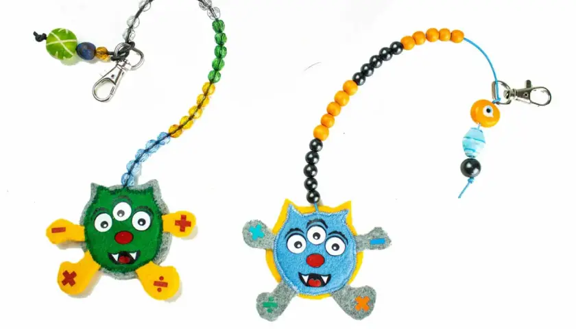 Zwei lustige Monster-Anhänger mit Perlenketten zum **rechenkette basteln**. Ein grünes und ein blaues Monster mit mathematischen Symbolen an den Füßen.