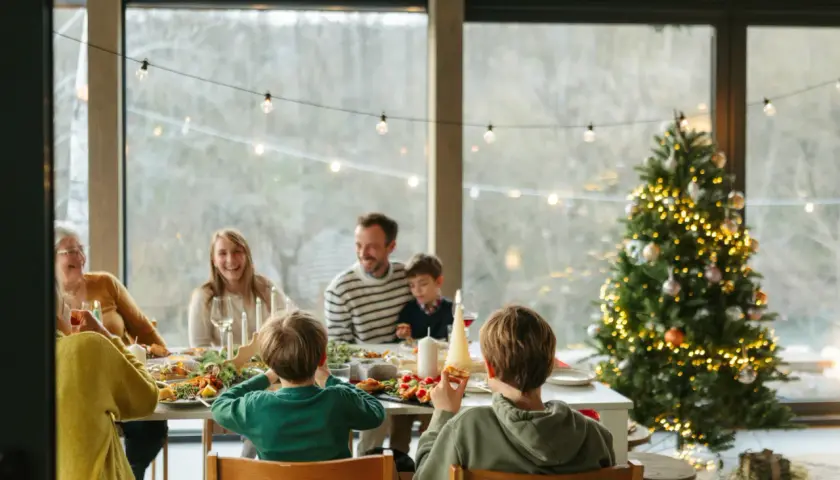 Familie feiert Weihnachten am festlich gedeckten Tisch, mit geschmücktem Baum im Hintergrund.