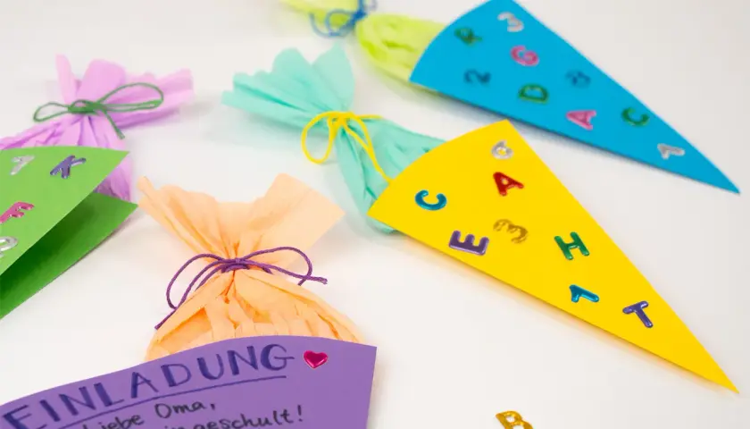 Bunte Schultüten und eine Einladung zum Einschulungsfest basteln. Kleine Buchstaben und Zahlen zieren die Tüten.