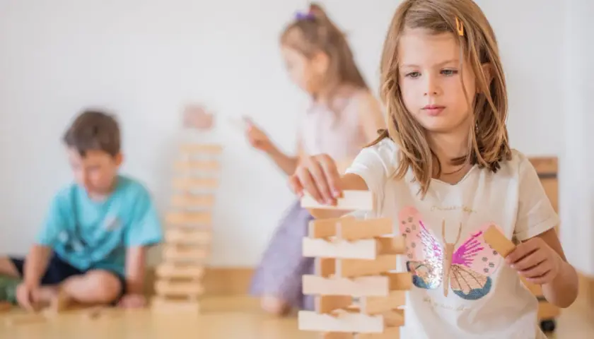Kinder bauen in der Bauecke im Kindergarten einen hohen Turm aus Holzklötzen.