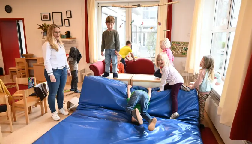 Kinder genießen spielzeugfreie Zeit in der Kita, klettern und toben auf einer blauen Matte.