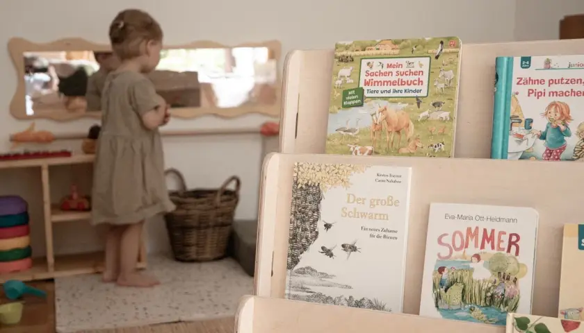 Ein kleines Mädchen in einer Montessori Kita entdeckt Bücher über Tiere und den Sommer.