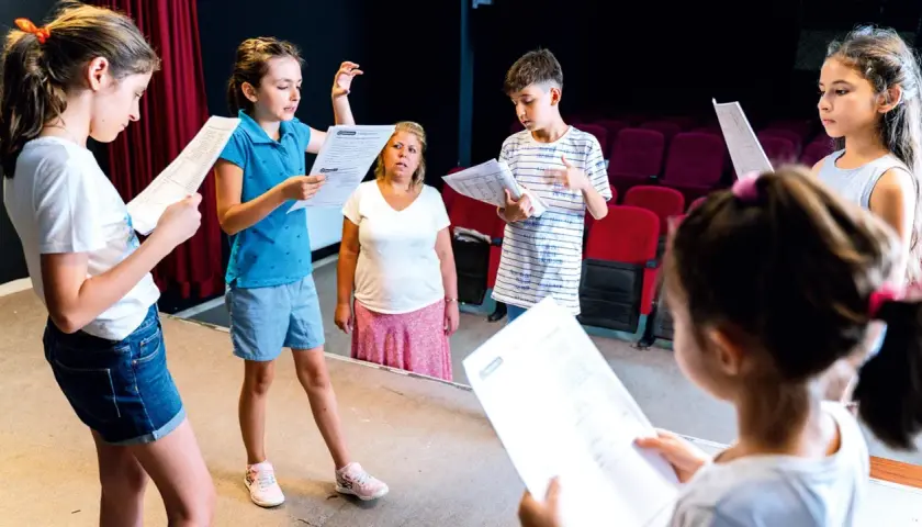 Kinder üben für ein **Vorlesetheater Grundschule**. Sie halten Texte in der Hand und schauen konzentriert.