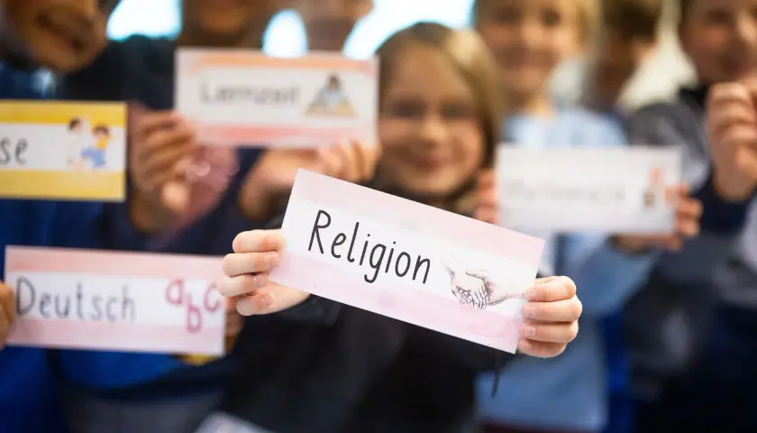 Kinder der Grundschule halten Schilder hoch, eines davon mit "Religion" beschriftet. Sie lernen über verschiedene Fächer, vielleicht im Rahmen der Fastenzeit.