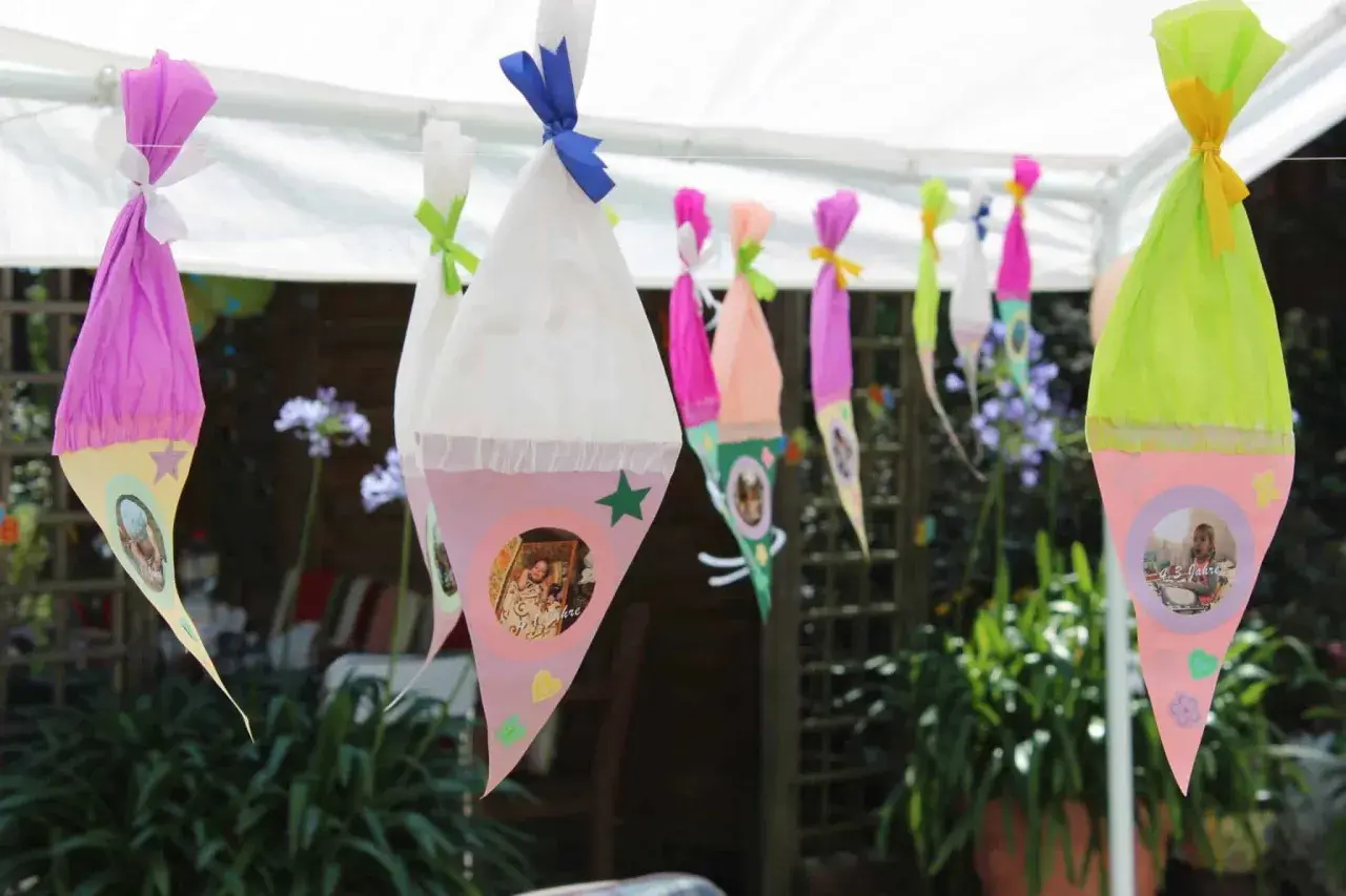 Bunte Zuckertüten mit Fotos hängen im Garten. Perfekte Spiele zur Einschulung im Garten für einen unvergesslichen Tag.