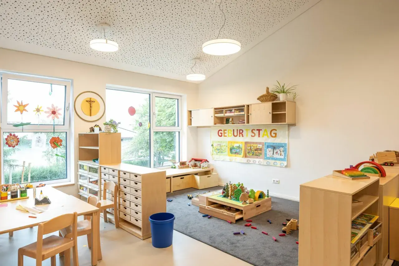 Helle, kindgerechte Reggio Raumgestaltung Kita mit Holzelementen, Spielzeug und einem Geburtstagsbanner.