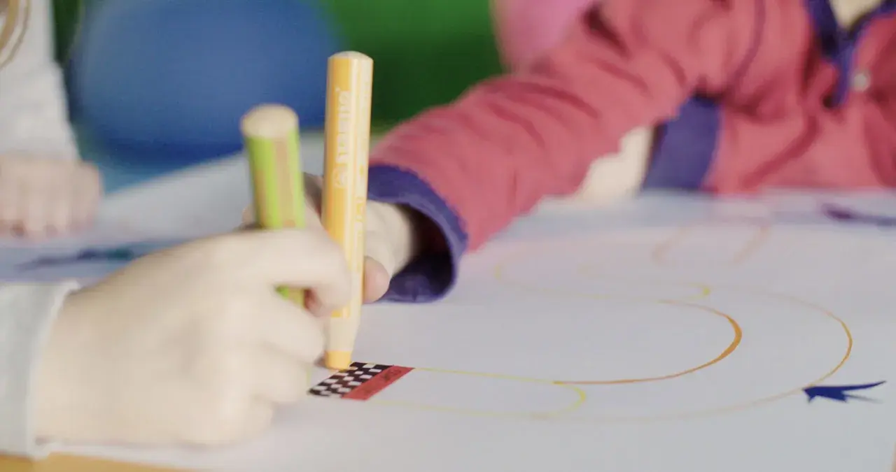 Kinder üben das Schreiben und Malen mit bunten Stiften auf einem großen Blatt Papier.