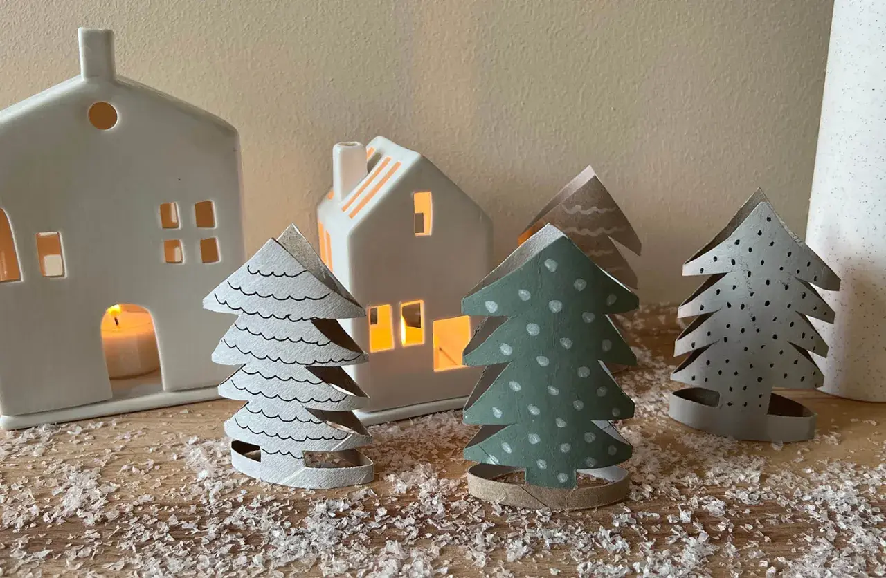 Kleine Weihnachtsbäume aus Papier, die Kinder basteln könnten, stehen vor leuchtenden Häusern.