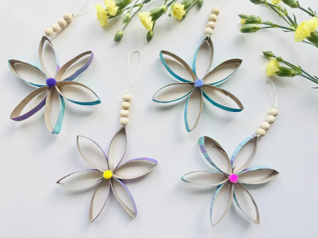 Blumen aus Klopapierrollen: basteln mit Klopapierrollen einfach. Bunte Blüten mit Holzperlen und Pompons, daneben gelbe Blumen.